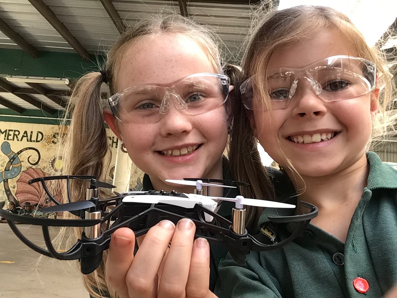 two smiling school girls wearing safety glasses and holding a micro drone